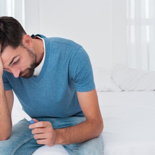 man-happy-about-pregnancy-test-result (1) A man sits on a bed, resting his head in his hands, conveying a sense of distress or deep contemplation.